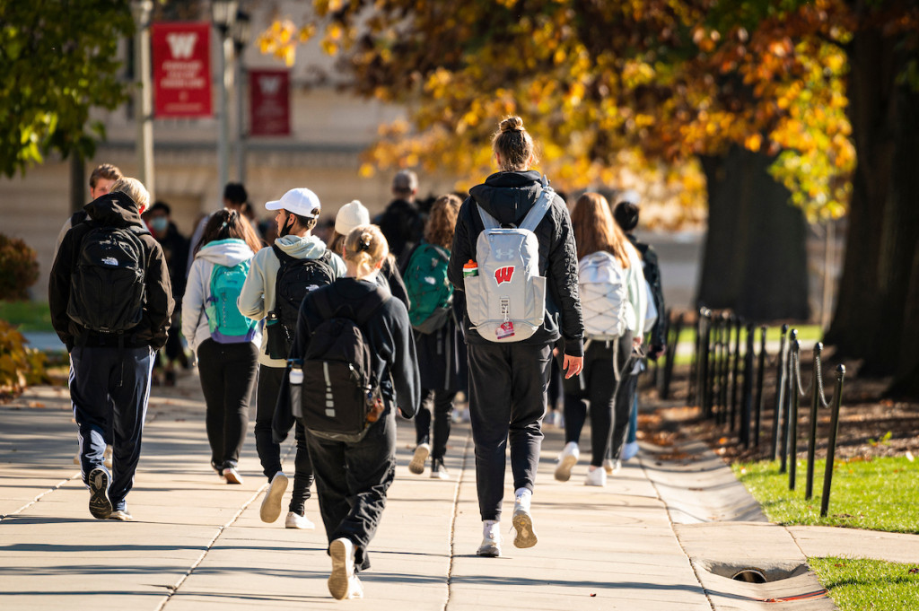 Some students wearing sweatshirts and backpacks walk on a sidewalk.