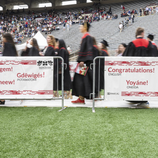 A line of graduates is seen behind a fence with writing on it.
