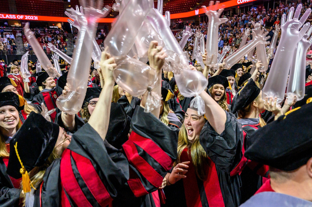 Students in graduation robes wave clear plastic inflated gloves.