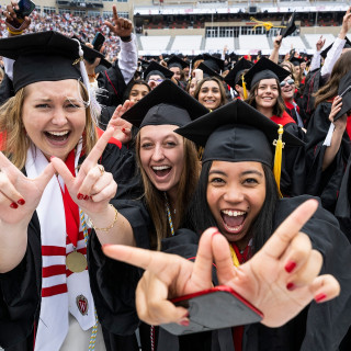 Graduates hold their hands in a W shape while smiling and laughing in Camp Randall Stadium.