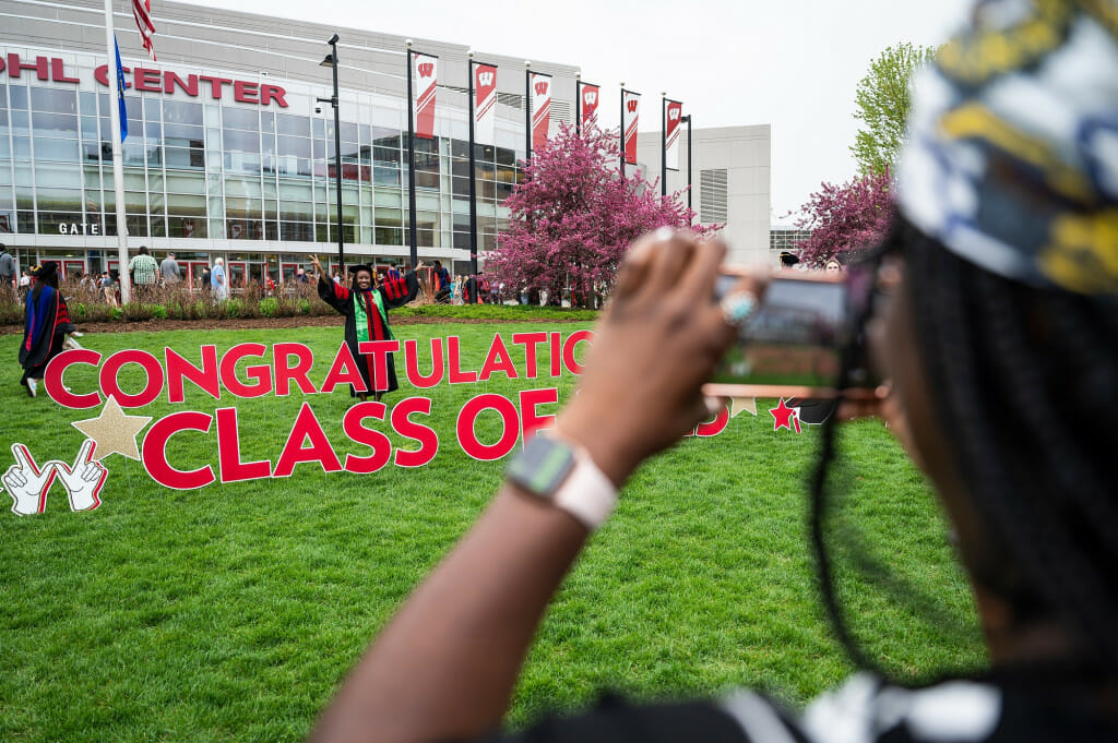 Graduate Adati Tarfa, soon to earn a doctoral degree in Health Services Research in Pharmacy, poses for photo with Class of 2023 signage outside of the Kohl Center at the University of Wisconsin–Madison