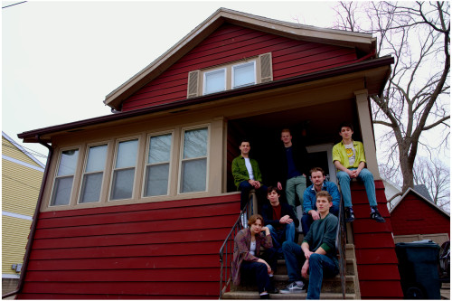 A group of people gather on the porch of a red house.
