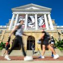 Several students walking quickly past Bascom Hall under a banner of Bucky Badger