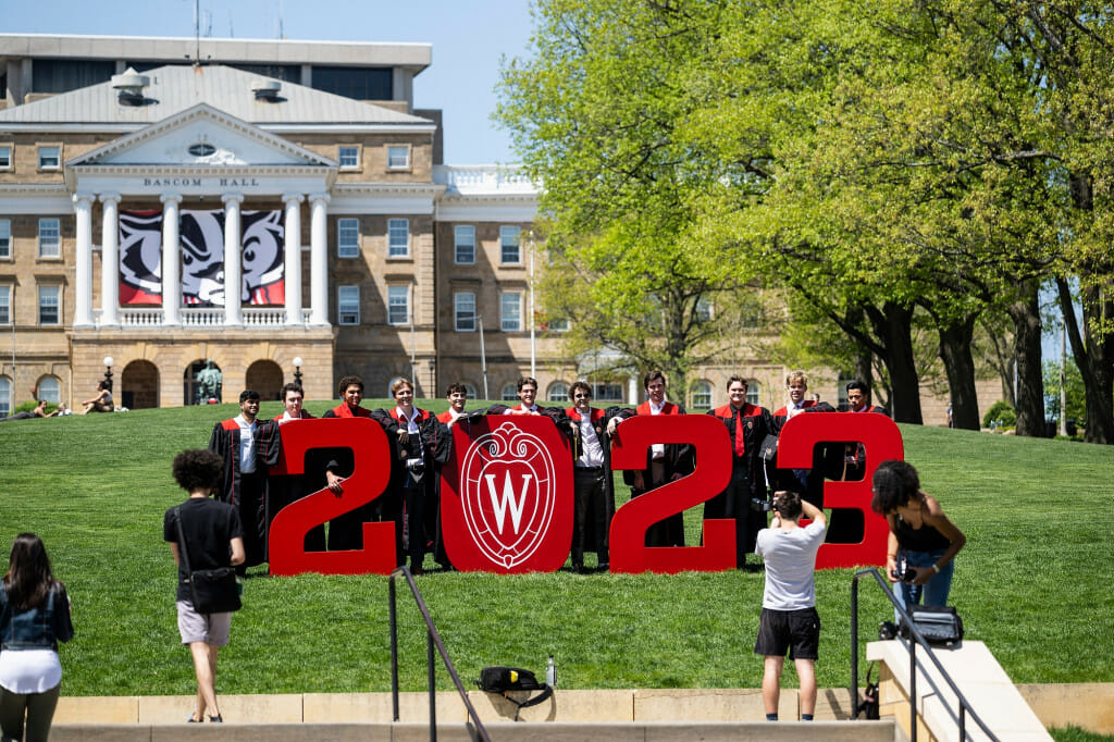 People wearing graduation robes pose amid the numbers 2023 on Bascom Hill.