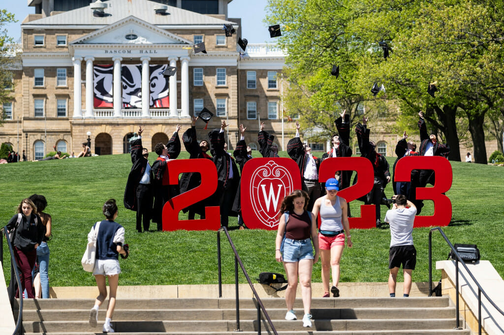 People wearing graduation gowns pose amid big red 2023 numbers on Bascom Hill.