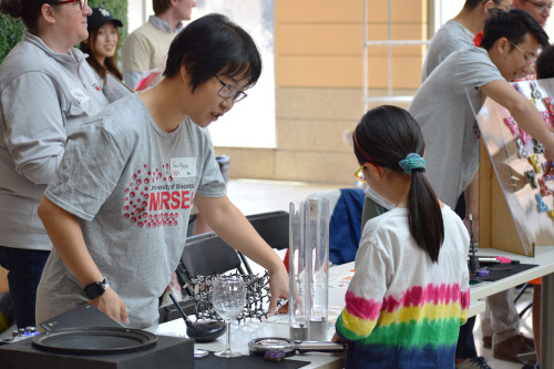 Post-doctoral researcher Soohyun Im speaks with a young visitor to her table at a materials science outreach event.