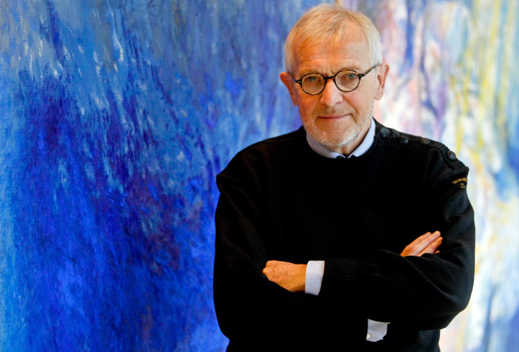 A photo portrait of Francis Halzen standing in front of a blue abstract mural