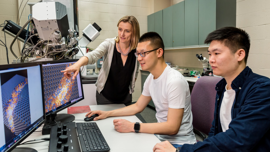 Professor Izabela Szlufarska (standing), and graduate students Xuanxin Hu (middle) and Nuohao Liu (right) gather around a computer monitor to discuss their research findings.