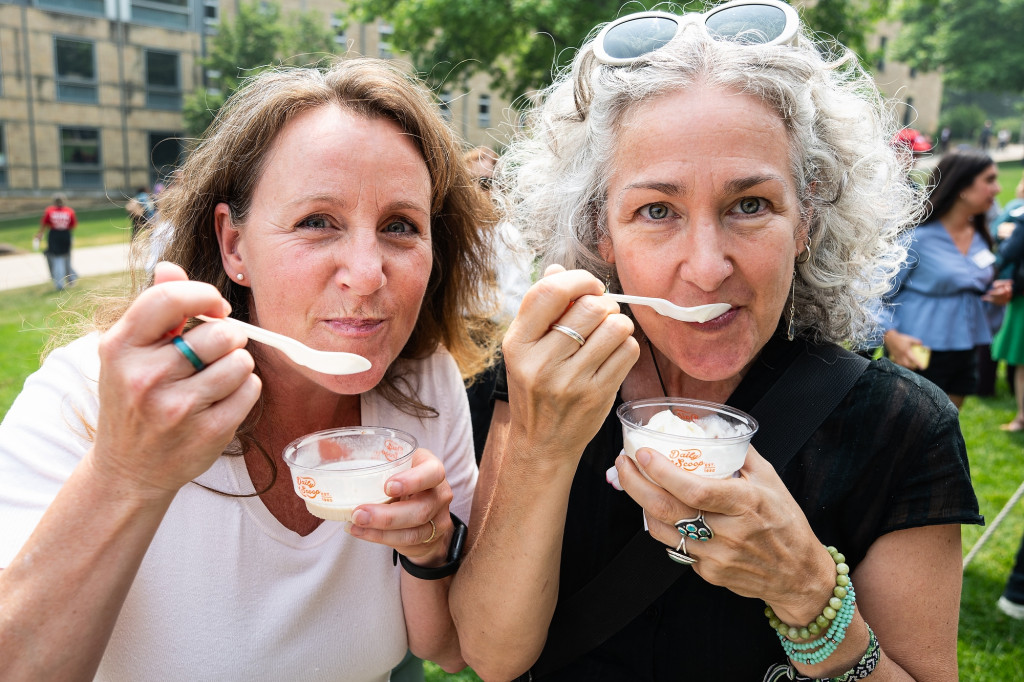 Two women at the ice cream social smile while taking bites of ice cream.