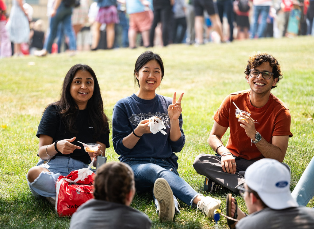 Three people sit on Bascom Hill eating ice cream from cups and smiling at the camera.