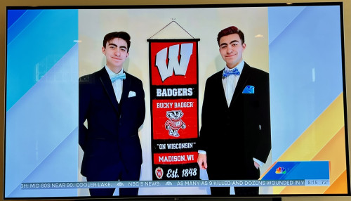 Two young man dressed in suits stand with a University of Wisconsin pennant between them.