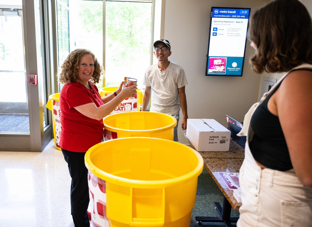 Indoors, Chancellor Jennifer Mnookin smiles while talking to two volunteers staffing a food pantry drive.