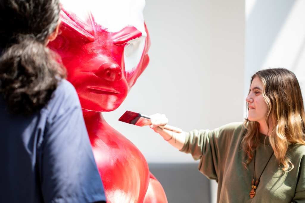 A person applies red paint to a white Bucky statue.