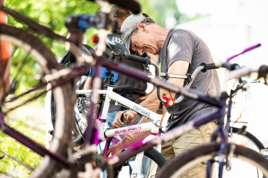 A man uses a wrench to work on a bicycle while outside on a sunny day.