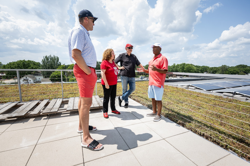 Four people stand in conversation on a green rooftop.