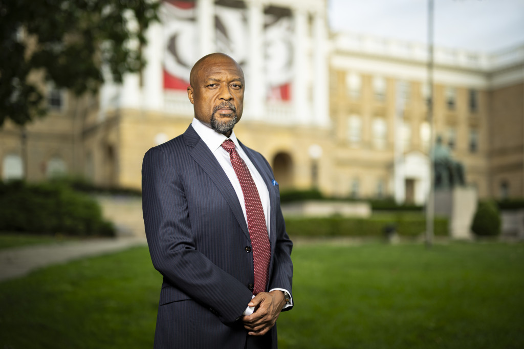 A man in a suit stands in front of a stone academic building.