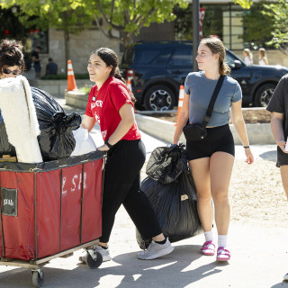 A student and a Badger Buddy push a red cart full of belongings.