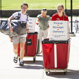 Three people push red carts filled with students' belongings outside Witte Residence Hall.