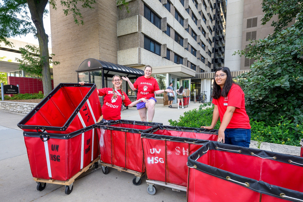 People in red t-shirts stand with red carts in front of a residence hall.