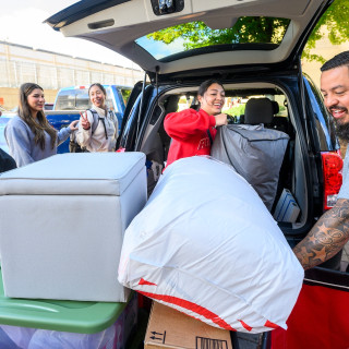 People work together to unload belongings from a car outside a residence hall.