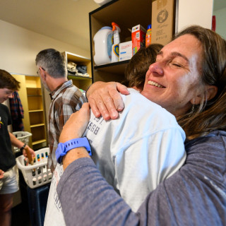 A mom gives her son a hug in his dorm room.