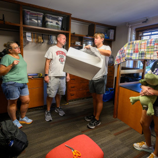 A group of people unpack boxes in a dorm room.