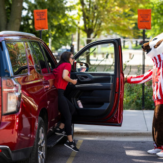 Bucky Badger opens the car door for a woman arriving for move-in day.