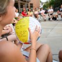 A young woman sits in a circle of fellow incoming first-year students on a stone patio. She is holding a beach ball covered with ice breaker questions.