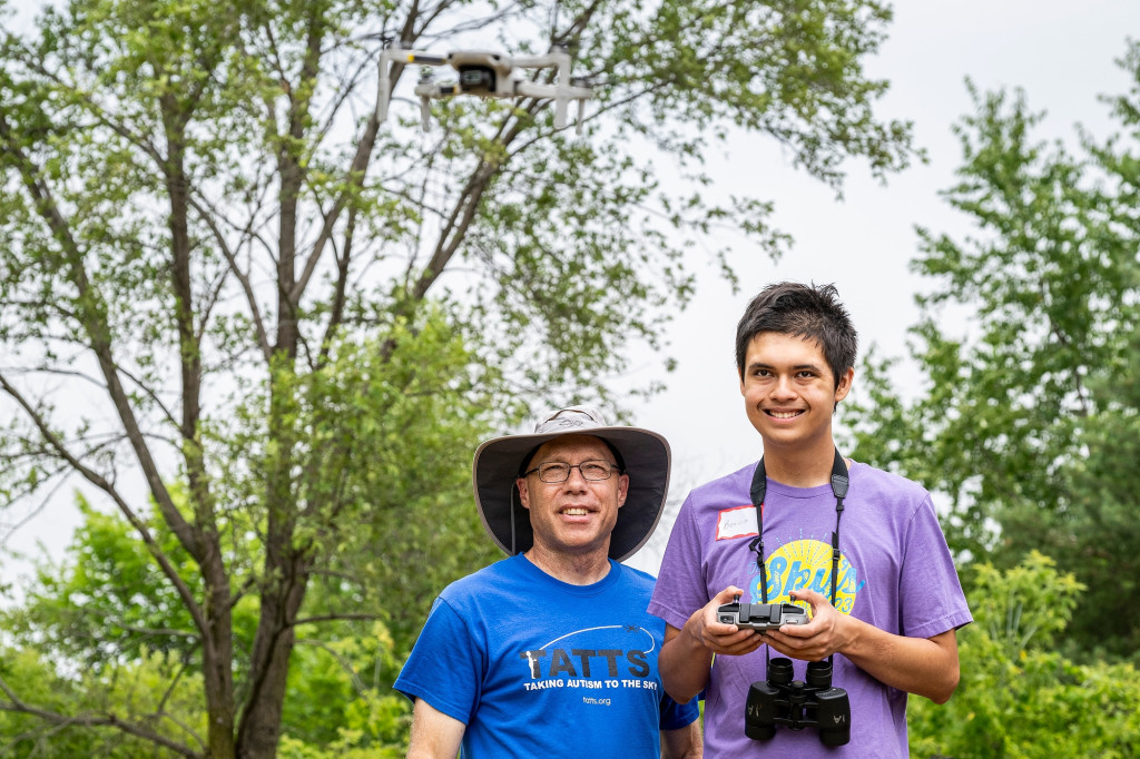 A man helps a boy use a drone remote, as they stand in a field.