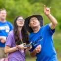 Two people operate a remote control and look up into the sky.