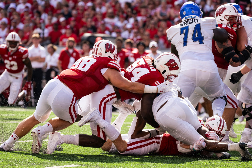 Three players in red tackle a player in white.