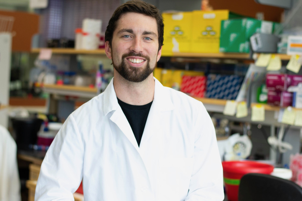 A portrait photo of Cason King wearing a white lab coat and standing in a laboratory.
