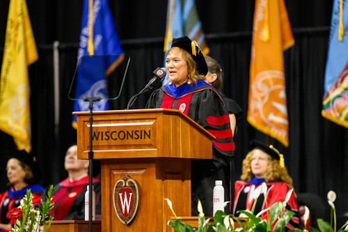A woman wearing academic robes speaks from a lectern.