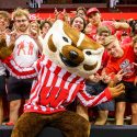 Bucky Badger poses with a large group of students who lean in to fill the frame.