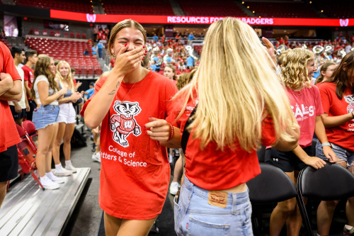 Two women wearing red shirts laugh as they dance together on the floor of the arena.