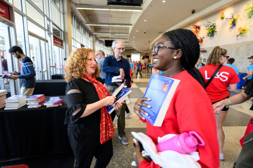 Chancellor Mnookin stands in the lobby of the Kohl Center handing out books to students.