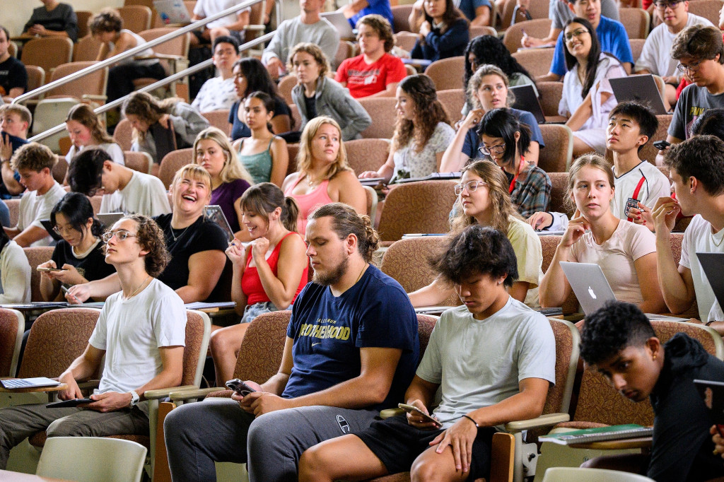 A view across full rows in a lecture hall as students take notes and listen.