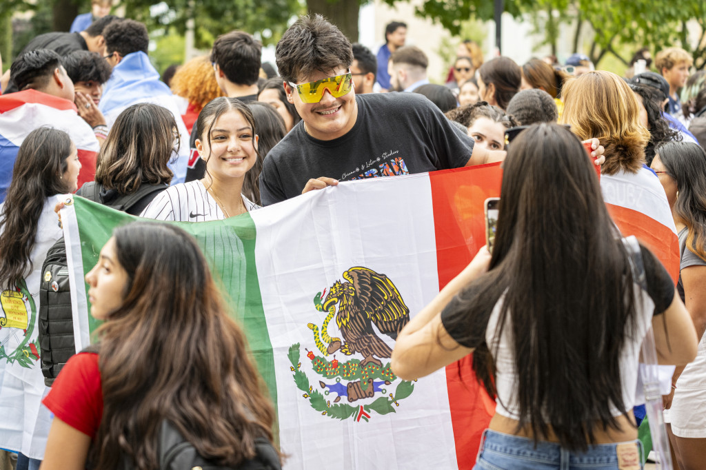 Some smiling people hold up the Mexican flag.