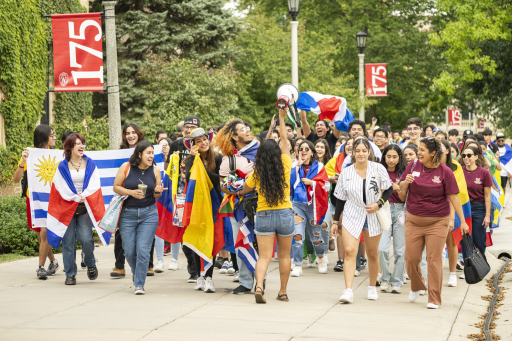 A group of students dance and walk up Bascom Hill carrying flags from Latin American countries.