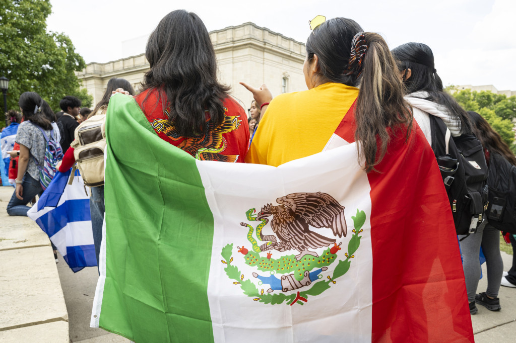 Two women hold the Mexican flag around them like a blanket.