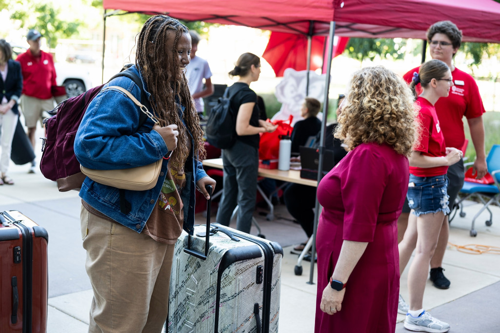 Pictured from behind, Chancellor Mnookin speaks with a new student pushing a suitcase outside a residence hall.