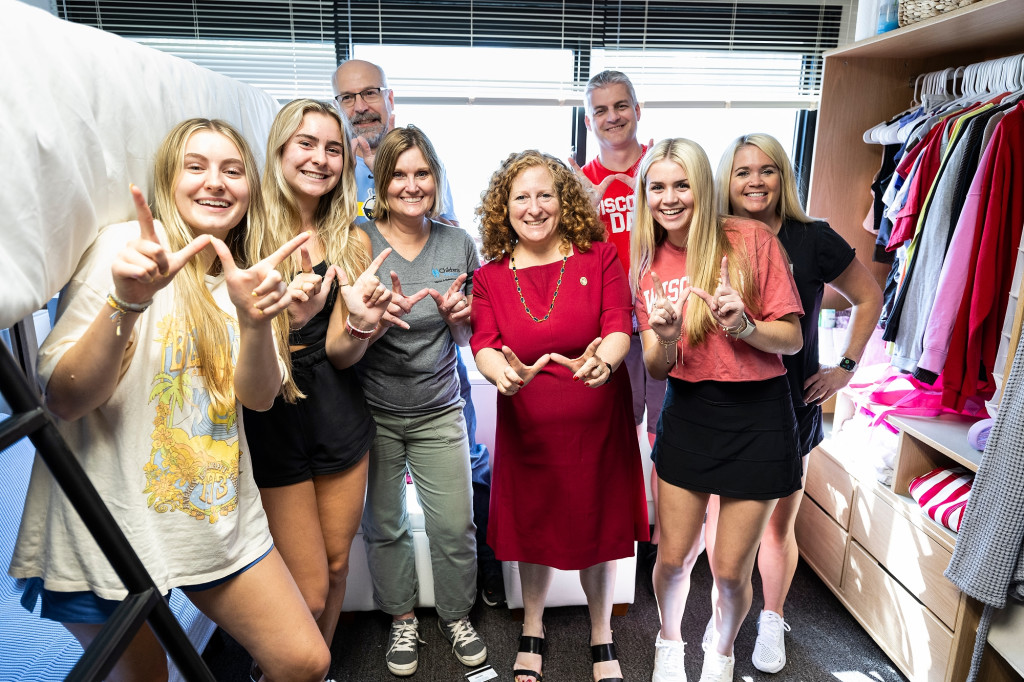 Chancellor Mnookin stands with students and their families in a dorm room. They're all making a W sign with their hands and smiling at the camera.