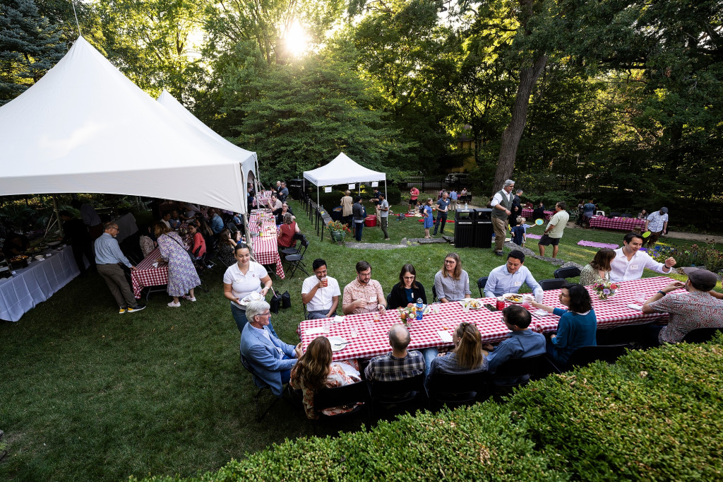 A wide view of people sitting and eating at picnic tables on the lawn at Olin House.