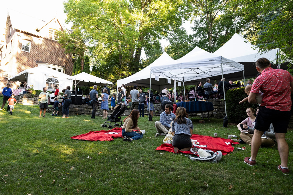 A wide shot of the lawn at Olin house is covered with picnic tents. People are milling about or sitting on the grass.