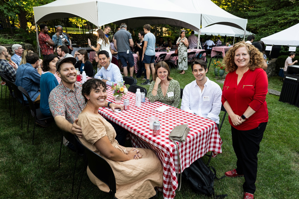 Several people sitting around a picnic table turn toward the camera and smile.