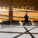 People walkl through the lobby of a building on the UW campus. Along a high, wood-paneled wall is the word research in capital letters.