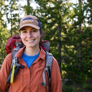 Arielle Link smiles for a portrait while carrying a large red backpack before heading into the lodgepole pine forest behind her.