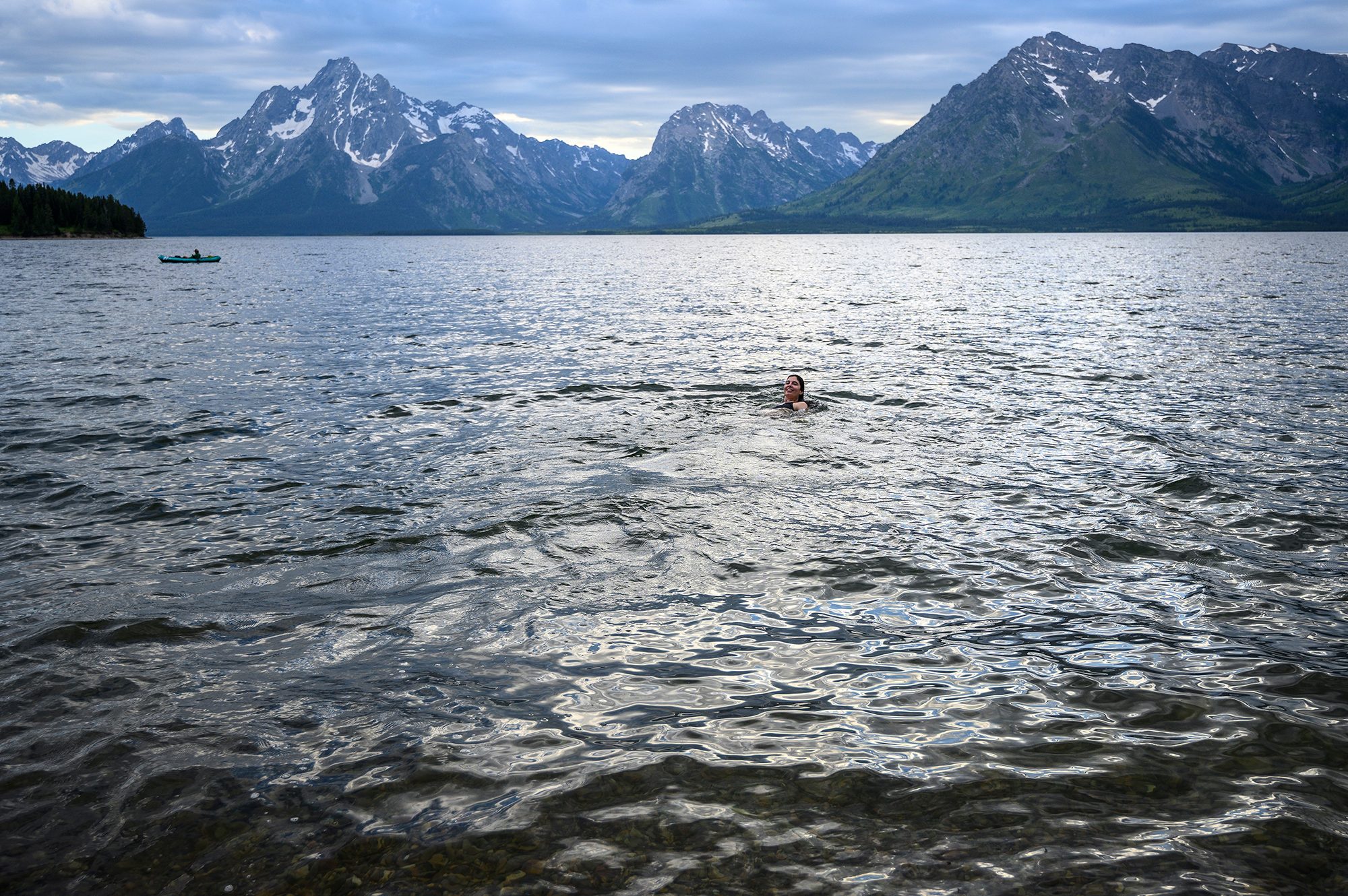 Stretching out at the base of the dramatic Tetons in various hues of blue are the calm waters of Jackson Lake. It's an overcast day but Arielle Link's head can be seen poking up from the water, bobbing along and smiling in the middle of the frame.