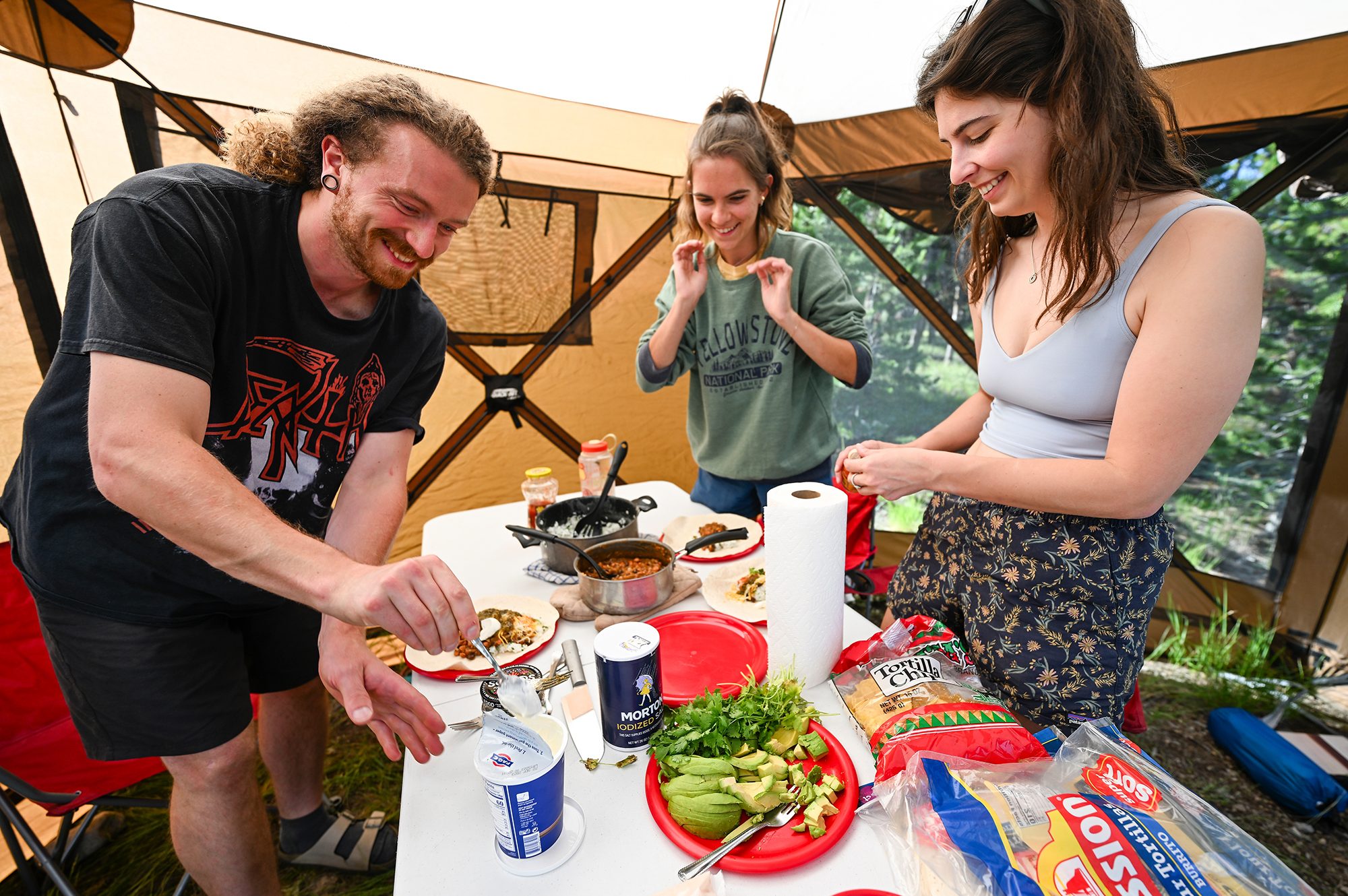 In a large brown tent beside the RV, Timon Keller, Lucy McGuire and Arielle Link add condiments to their burrito dinner. The researchers all look excitedly at the collapsible table before them which is full of sliced avocado, cilantro, sour cream, tortillas, chips, salsa, rice and beans.