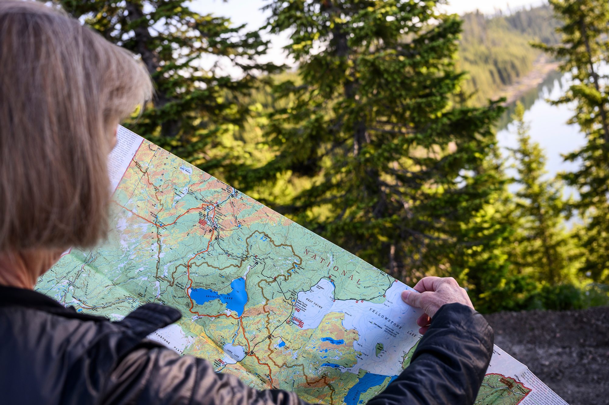 A woman holds up a map while a lake surrounded by evergreen trees is seen in the background.